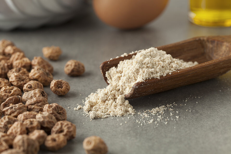 Erdmandeln gemahlen und ganze Erdmandeln. Gemahlene Erdmandeln auf Löffel neben ganzen Erdmandeln, gut geeignet für basenbetonte Rezepte.