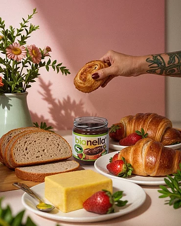 Bionella ab sofort in allen dm Filialen erhältlich. Gedeckter Tisch mit bionella, Butter, Brot, Croissants. In der Hand ein Croissants.
