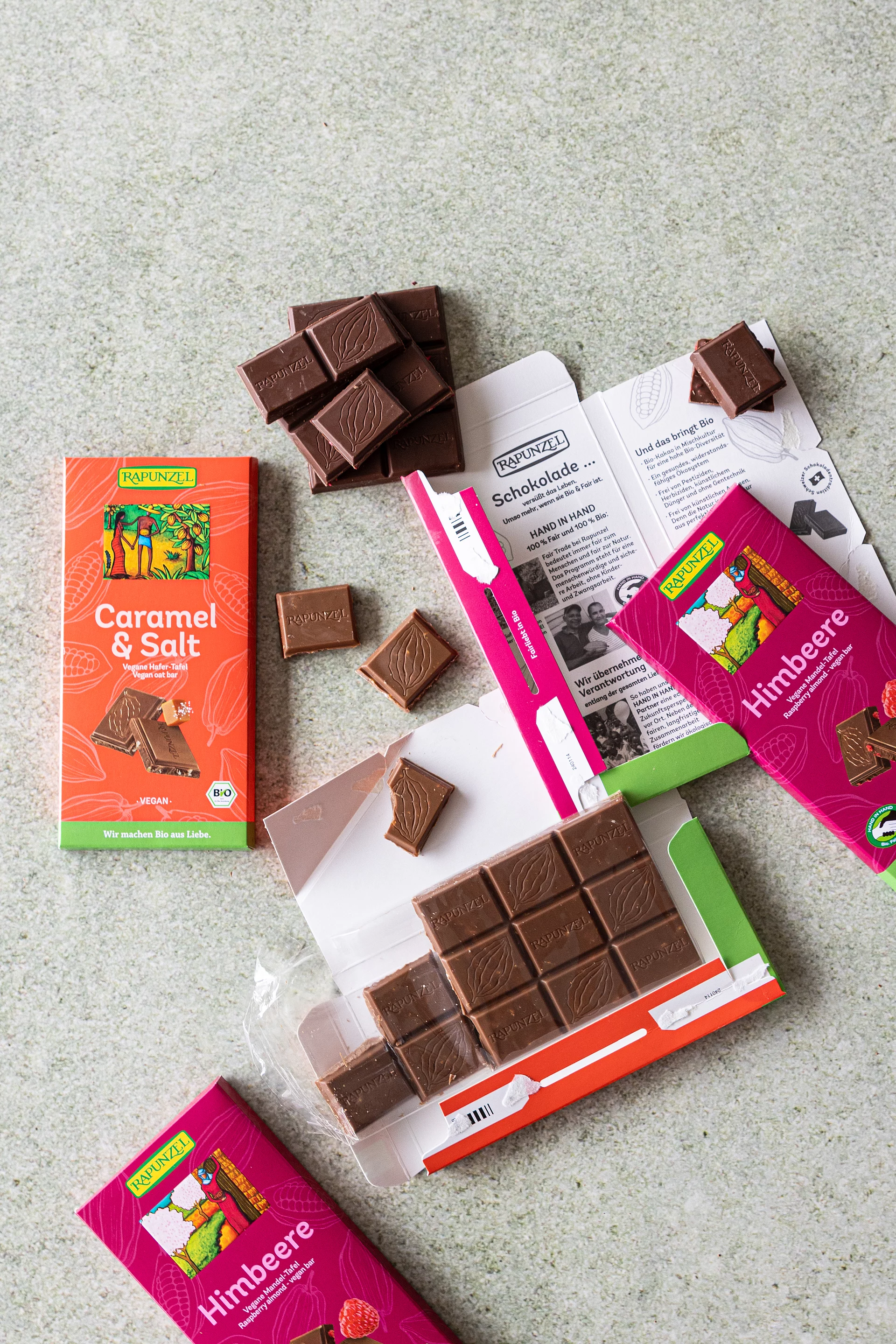 Vegane Schokoladen: Caramel Salz und Himbeer Schokolade. Auf einem Tisch liegen mehrere Sorten veganer Rapunzel Schokolade.