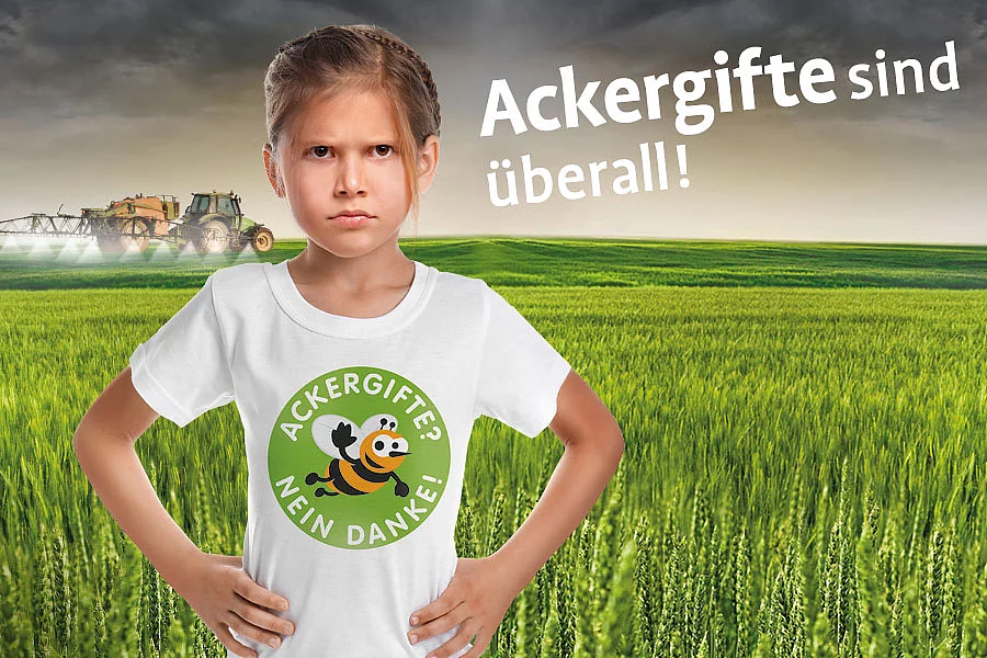 Ackergifte? Nein Danke! Hauptmotiv Auf dem Kampagnenbild, zu Ackergifte? Nein Danke! steht ein verärgertes Mädchen auf einem Feld, auf dem im Hintergrunde ein Pestizid versprühender Traktor im Einsatz ist.