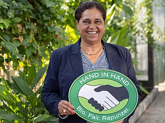 Gründerin Samia Chibani zu Besuch bei Rapunzel in Legau. Firmengründerin Samia Chibani mit einem HAND IN HAND-Schild im Tropenhaus bei Rapunzel in Legau.