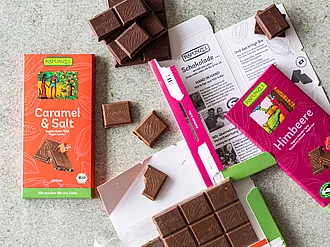 Vegane Schokoladen: Caramel Salz und Himbeer Schokolade. Auf einem Tisch liegen mehrere Sorten veganer Rapunzel Schokolade.