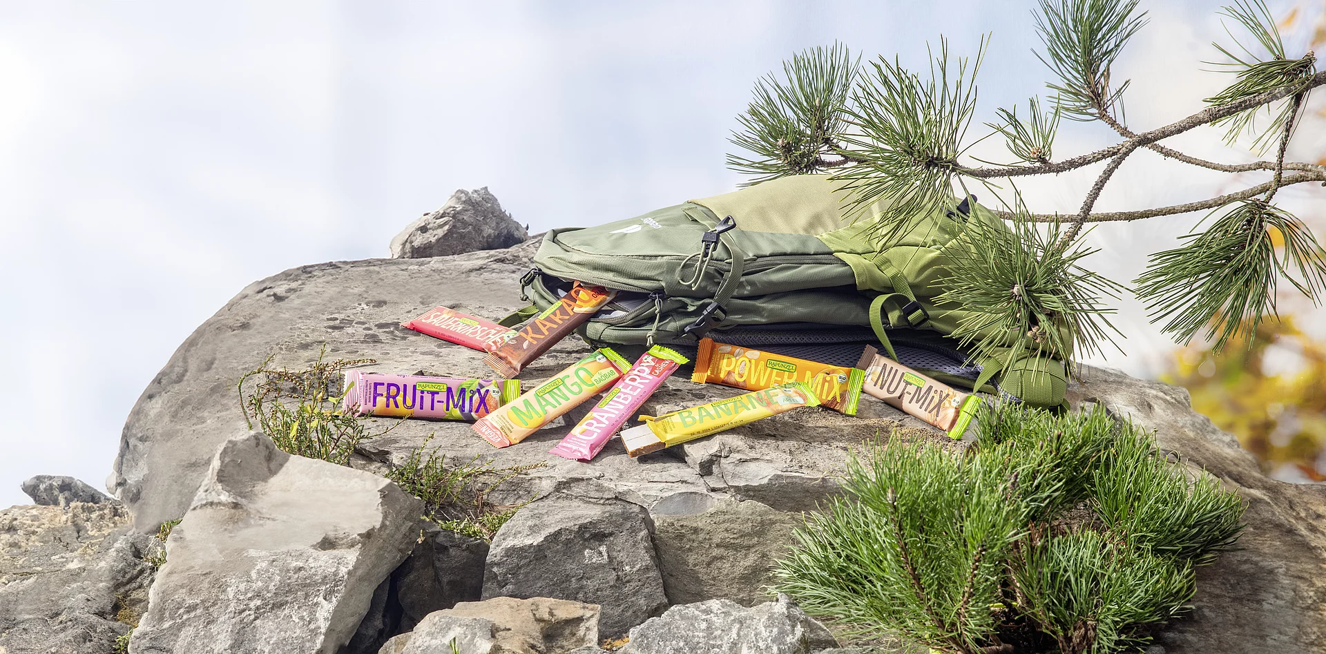 : Rapunzel Fruchtschnitten auf einem Felsen. Auf einem Felsen liegt ein Wanderrucksack, aus dem Rapunzel Fruchtschnitten herausgefallen sind.