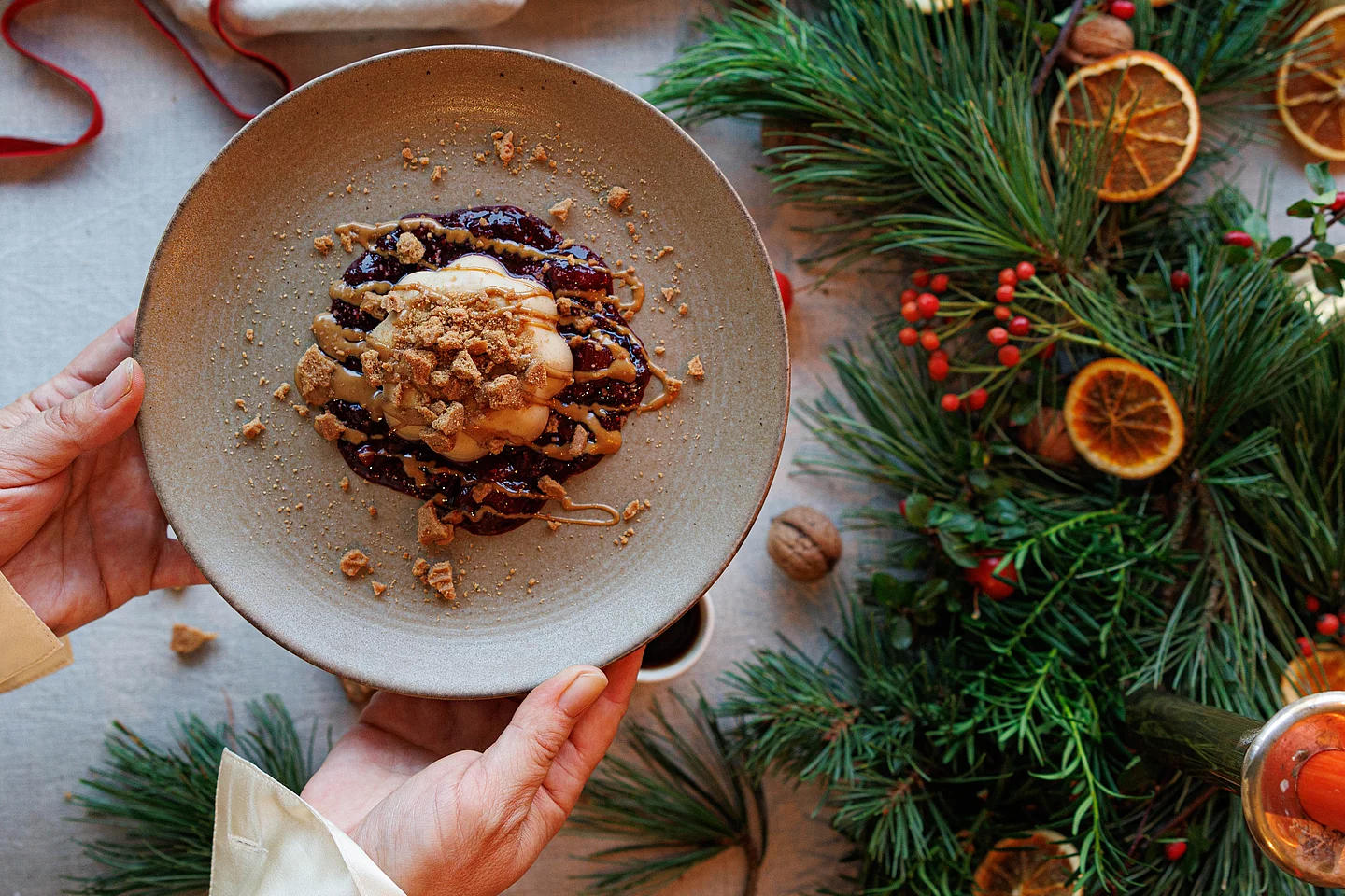 pekulatius-Panna-Cotta mit Beerensauce für festliches Weihnachtsmenü. Spekulatius-Panna-Cotta mit Beerensauce, angerichtet auf Teller neben weihnachtlichem Tannengrün mit getrockneten Orangenscheiben.