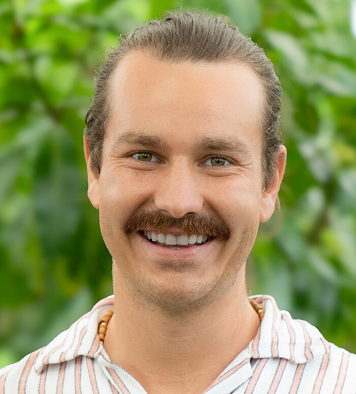 Manuel Kämmerle Rapunzel Mitarbeiter steht vor blühender Pflanze.