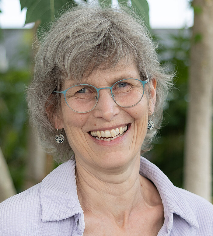 Anke Malas Porträt von Anke Malas, Mitarbeiterin im Rapunzel Kundenservice, lächelnd vor Pflanzen im Tropenhaus.