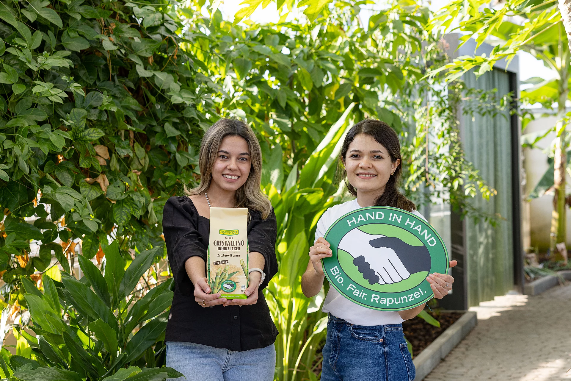 HAND IN HAND-Partner Manduvira mit Zuckerrohr. Die Leiterinnen des HAND IN HAND-Partners Manduvira mit Zuckerrohr, einer Packung Rohrzucker und dem HAND IN HAND-Logo.