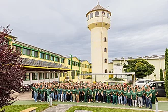 Über die Hälfte aller Produkte fertigen unsere Kolleginnen und Kollegen vor Ort in Legau. Gruppenfoto von Rapunzel Mitarbeitenden vor dem Unternehmensgebäude und dem Rapunzel Turm.